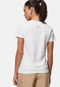 Hvid bomulds T-shirt med korte ærmer, der har et orange "COOL MOMS CLUB" print på ryggen. Glat tekstur og klassisk pasform.