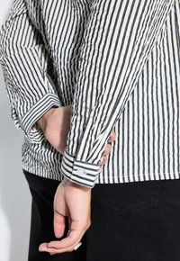 Gestreept overhemd met knopen in wit en zwart, met een gerimpelde textuur, contrasterende manchetten en knoopdetail aan de pols.