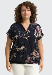 Marineblaue Bluse mit kurzen Ärmeln, ausgestattet mit einer durchgehenden Knopfleiste, übergroßer Passform sowie lebhaften rosa und grünen Blumenmustern.