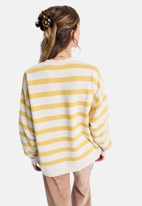 Übergroßer Sweatshirt in Creme mit gelben horizontalen Streifen, geripptem Halsausschnitt und Bündchen. Der Stoff ist weich und strukturiert.