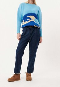 Ljusblå stickad tröja med vågmönster i blått och beige, tillsammans med mörk denim-byxor med hög midja och bruna mocka ankelskor.