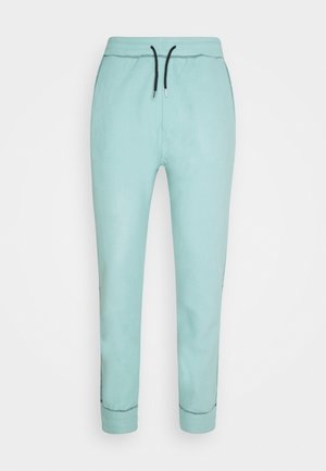 Pantalon de jogging bleu clair avec taille à cordon noire et détails visibles des coutures aux poignets et sur les côtés, présenté sur fond blanc.