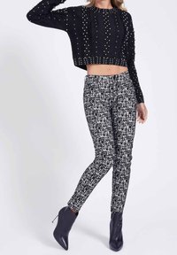Czarny krótki sweter z fakturą i metalowymi ćwiekami, zestawiony z czarnymi i białymi spodniami o dopasowanym kroju oraz czarnymi botkami na kostkę.