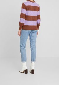 Brun och lavendelfärgad randig tröja med ribbad nederkant, kombinerad med ljusblå denimjeans och vita klackstövletter.