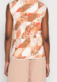 Chaleco acolchado sin mangas con un diseño de patchwork en cálidos tonos de naranja, marrón y crema, con patrones florales y geométricos.
