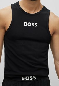 Svart tanktop i bomull med ordet "BOSS" i vitt på framsidan och midjan, med en figurnära design och ärmlös skärning.