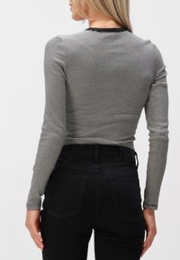 Haut à manches longues rayé noir et blanc avec un col rond. Le tissu est moulant, avec une texture lisse et un col noir contrastant.