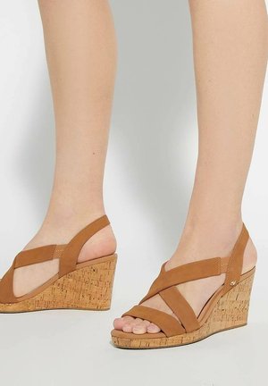 Sandales en cuir marron à talon compensé en liège, avec des brides croisées et un design à bout ouvert. La hauteur du talon est modérée.