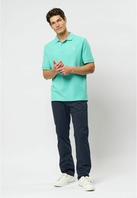 Pikétröja i akvagrön, tillverkad av bomull, med krage och en liten logotyp. Kombineras med marinblå byxor och vita sneakers.