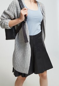 Gray textured cardigan over a light blue tank top, paired with a black flared leather skirt and a black bag with adjustable straps.