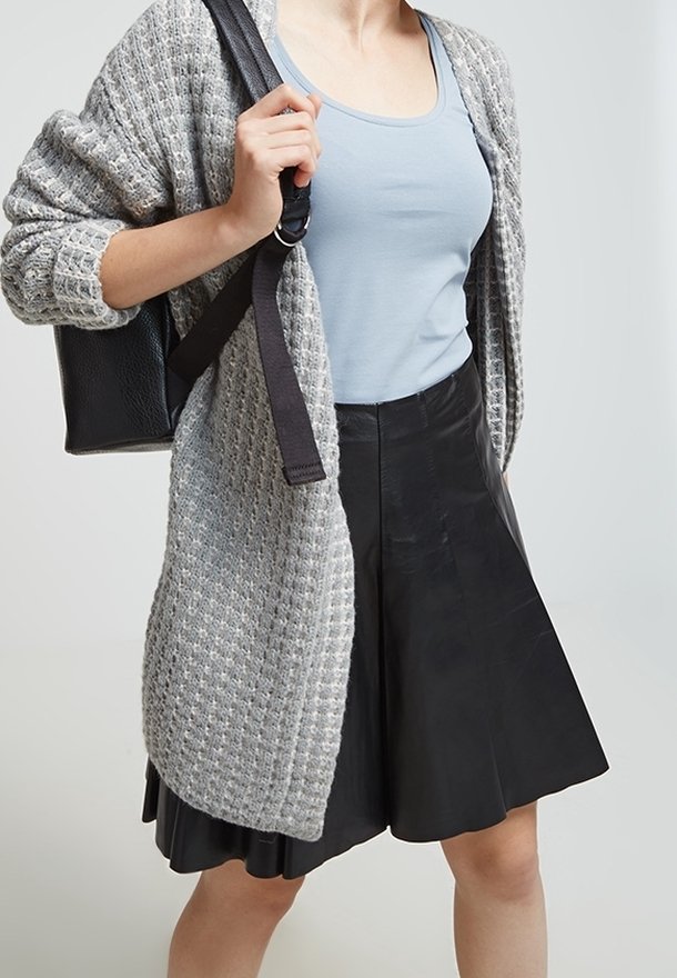 Gray textured cardigan over a light blue tank top, paired with a black flared leather skirt and a black bag with adjustable straps.