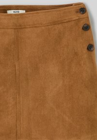 Jupe trapèze en daim marron avec quatre boutons foncés sur le côté et des coutures discrètes, offrant une texture douce et une finition soignée.