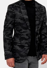 Czarny i szary blazer w kamuflażu z dopasowanym krojem, strukturalną tkaniną, klapami typu notch i zapięciem na dwa guziki. Połączony z czarną koszulą.
