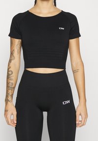 Svart kortärmad träningslinne med texturerade paneler, kombinerat med svart högmidjade leggings som har en logotypdetalj.