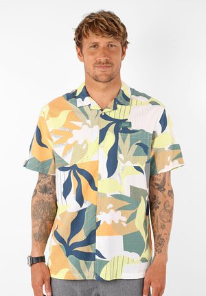 Chemise à manches courtes avec un motif de feuilles abstrait multicolore en vert, jaune et bleu sur un tissu léger.