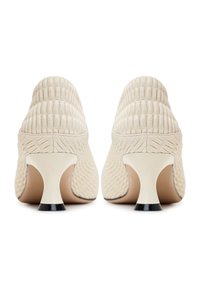 Chaussures à talons hauts beiges texturées avec un design strié, dos semi-découpé, et un talon blanc avec un embout noir. Surface lisse avec des coutures définies.