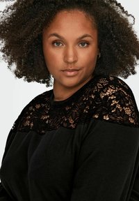 Sudadera negra con un panel de encaje negro decorativo en los hombros, con una textura suave y un corte holgado.