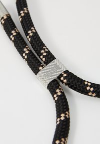 Μαύρο και μπεζ πλεξούδα σχοινιού με υφασμένο μεταλλικό κούμπωμα σε ασημί, που περιλαμβάνει χάραξη της μάρκας και σχέδιο με πλεξούδες.
