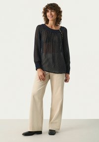 Blouse à pois navy, en tissu léger, col rond avec détail de bouton. Pantalons en velours côtelé crème à jambe large et chaussures noires.
