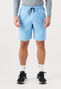 Man med ljusblå träningsshorts med svart dragsko, grå långärmad tröja, vita Nike-strumpor och svarta Nike löpskor.