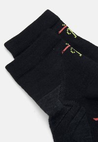 Schwarze Socken mit gerippten Bündchen, strukturiertem Stoff und kontrastierenden Grafiken in Rot und Grün. Sie zeigen ein geometrisches Muster an den Seiten.