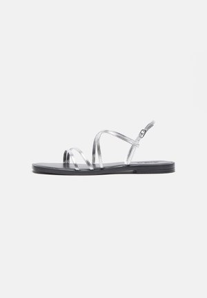 Silver strappy sandals with a flat black sole, featuring thin metallic straps and an adjustable ankle buckle. Smooth texture throughout.