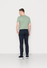 T-shirt vert à manches courtes, associé à un pantalon slim fit bleu marine. Modèle portant des baskets bleues marines, de dos face au spectateur.
