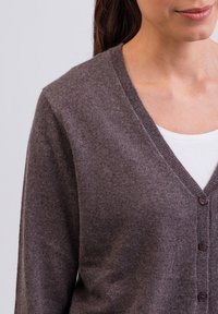 Mörkbrun cardigan med V-ringning, mjuk textur och femknappsstängning. Lätt tyg, diskret glans och figurnära ärmar.