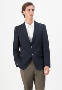 Temno moder blazer iz teksturiranega blaga, z dvema sprednjima žepoma, zarezanimi reverji in zapiranjem na dva gumba, v kombinaciji z belo srajco.