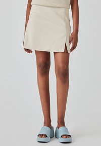 Jupe mini beige avec fentes sur les côtés. Le tissu semble doux et texturé. Associée à des sandales à plateforme bleues avec de larges brides.