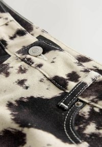 Gros plan d’un jean en denim tie-dye noir et blanc, focalisé sur la ceinture, le bouton et les détails de couture.