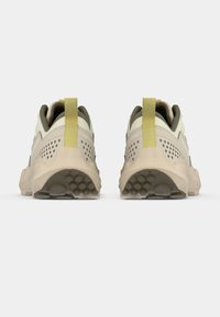 Οπίσθια όψη αθλητικών παπουτσιών με μπεζ σώμα, ελαιοπράσινες λεπτομέρειες, κίτρινη θηλιά έλξης και διάτρητα πλευρικά πάνελ για αερισμό.