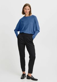 Pull bleu surdimensionné avec manches longues, associé à un pantalon noir cintré. La tenue présente une coupe décontractée et une texture lisse.