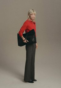 Suéter rojo de canalé, bolsa de tote negra con asas, pantalones oscuros acampanados y zapatos planos negros, sobre un fondo neutro.