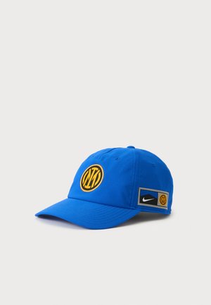 Cappellino da baseball blu con logo circolare giallo e nero sulla parte frontale e toppa con logo Nike sul lato su uno sfondo bianco uniforme.