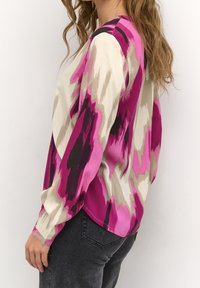 Blouse multicolore présentant un motif abstrait rose, noir et beige, manches longues, tissu lisse et coupe épaules tombantes.