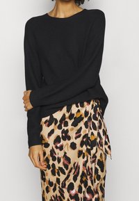 Pull noir en tricot avec un col rond, assorti à une jupe beige ornée d'un imprimé léopard audacieux en noir, rose et accents marron.