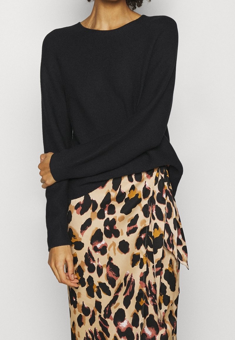 Pull noir en tricot avec un col rond, assorti à une jupe beige ornée d'un imprimé léopard audacieux en noir, rose et accents marron.