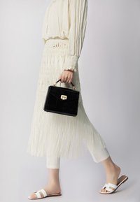 Borsa nera con texture a forma di coccodrillo e hardware dorato, abbinata a una gonna bianca con frange e sandali bianchi con la zeppa.