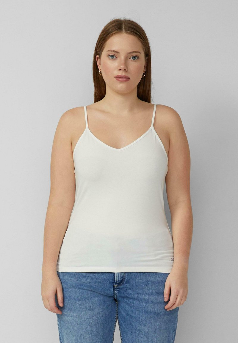 Witte, nauwsluitende camisole met dunne verstelbare bandjes en een v-hals, gemaakt van een gladde stof, gecombineerd met lichtblauwe spijkerbroek.