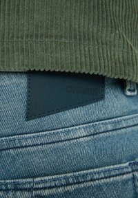 Vihreää ribbineulosta yläosassa ja sinistä denim-kangasta alhaalla. Näkyvät ompeleet ja suorakaiteen muotoinen nahkainen merkki, johon on painettu "CHASIN'".