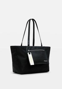 Black tote bag made of smooth fabric with two long straps, front zip pocket, and a white tag with text. Features minimalistic design.