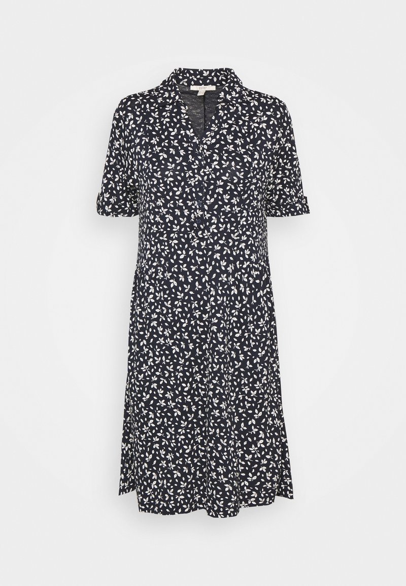 Granatowa sukienka do kolan z białym wzorem liści, krótkimi rękawami z podwiniętymi mankietami oraz kołnierzykiem z otwarciem w kształcie litery V.