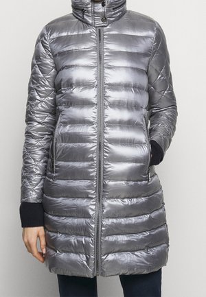 Sølvmetallic quiltet dunjakke med høj krave, frontlynlås, lynlåslommer i siderne og sorte strikkede ærmekanter, båret af en person.