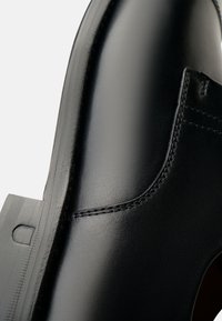 Stivale alla caviglia in pelle nera con texture liscia, forma curva, cuciture visibili e punta arrotondata con tacco basso.