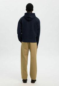 Sudadera con capucha de color azul marino y un corte relajado, combinada con pantalones de pierna ancha beige y zapatos negros, vista desde atrás.