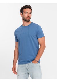 Modré tričko s krátkým rukávem z jemného materiálu, s kulatým výstřihem, jemnými švy a malým logem vyšitým na přední straně.