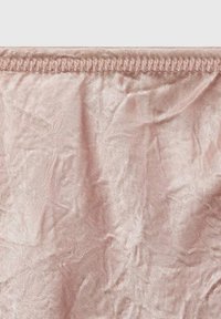 Gros plan d’un tissu rose pâle froissé avec un ourlet cousu le long du bord supérieur sur un fond blanc.
