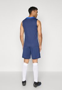 Débardeur de sport marin avec un col bleu, assorti à un short marine. Porter avec deschaussettes blanches hautes jusqu'aux genoux et des chaussures de football noires. Design simple.