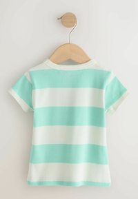 T-shirt côtelé à manches courtes pour tout-petit avec de larges rayures horizontales turquoise et blanches, suspendu sur un cintre en bois contre un mur uni.